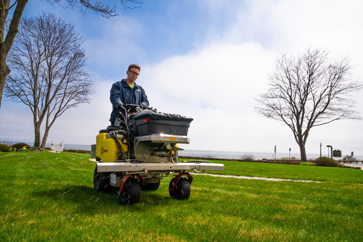 lawn care technician fertilizes grass with granular fertilizer