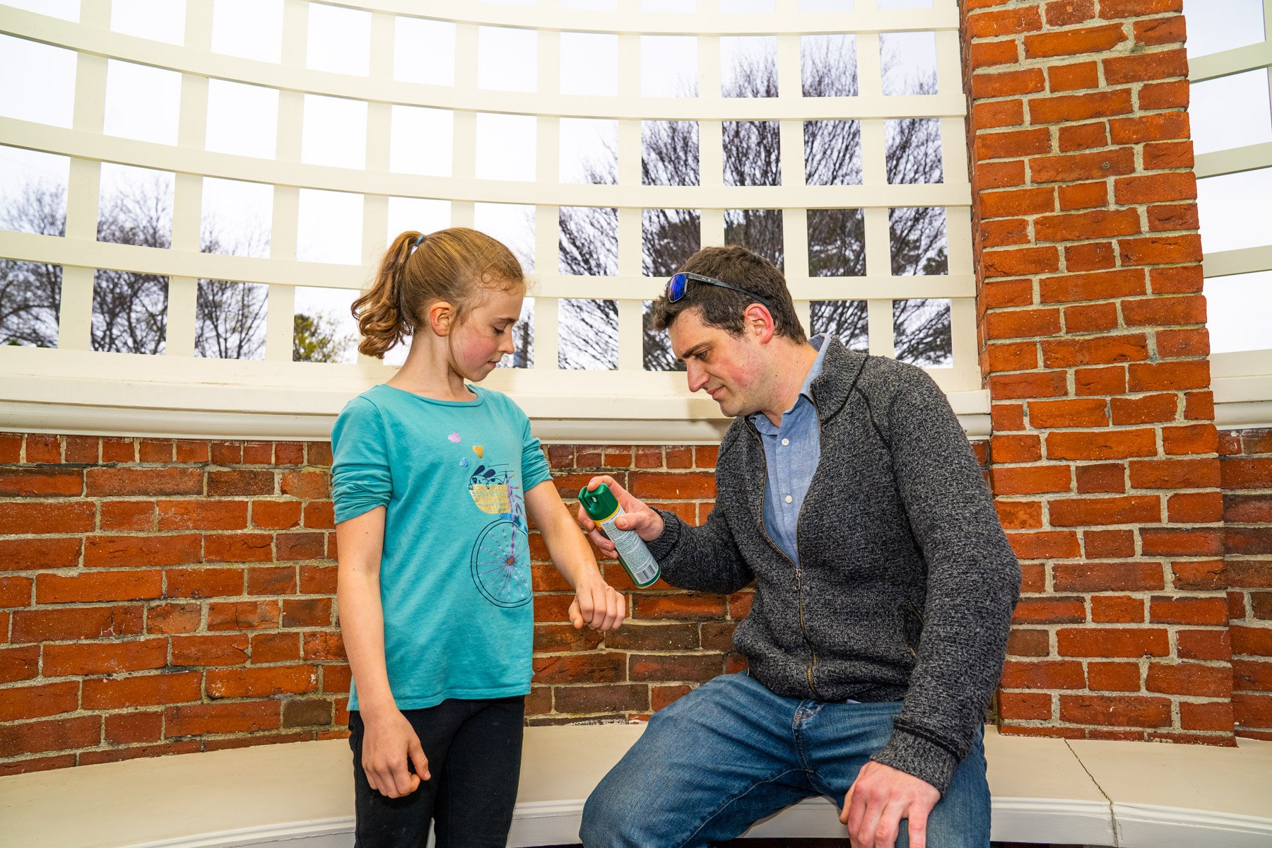 homeowner spraying child with deet bug spray
